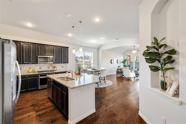 kitchen featuring sink, dishwasher, a kitchen island with sink, hanging light fixtures, and light stone countertops