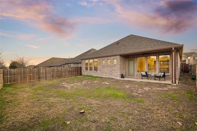 back house at dusk featuring a lawn and a patio