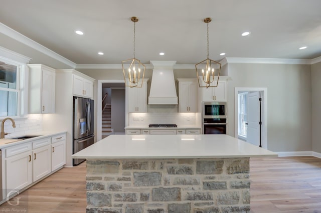 kitchen featuring white cabinets, appliances with stainless steel finishes, a kitchen island, sink, and custom range hood