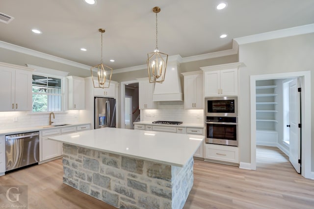 kitchen featuring custom exhaust hood, a center island, appliances with stainless steel finishes, hanging light fixtures, and sink