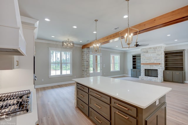 kitchen featuring a center island, a stone fireplace, crown molding, light hardwood / wood-style flooring, and pendant lighting