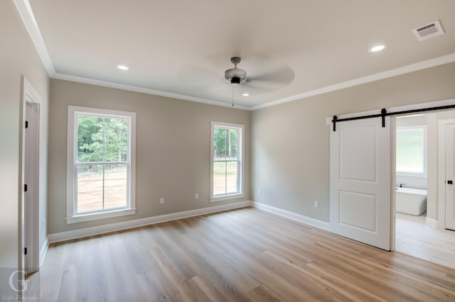 unfurnished room featuring ornamental molding, a barn door, and light wood-type flooring