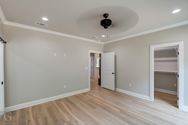 unfurnished bedroom with light hardwood / wood-style flooring, ceiling fan, a barn door, a walk in closet, and ornamental molding