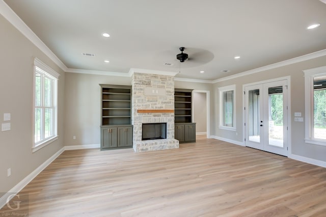 unfurnished living room featuring light hardwood / wood-style floors, built in shelves, ornamental molding, and a stone fireplace