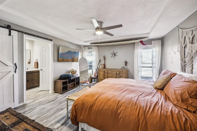 bedroom featuring a barn door, a textured ceiling, multiple windows, and light wood-type flooring