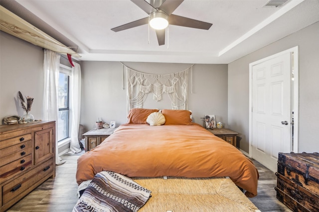 bedroom featuring hardwood / wood-style flooring, ceiling fan, and a tray ceiling