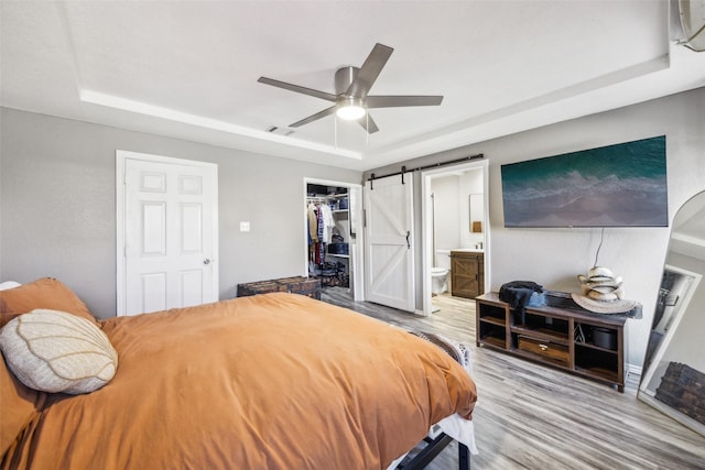 bedroom featuring connected bathroom, hardwood / wood-style flooring, a raised ceiling, a barn door, and a closet