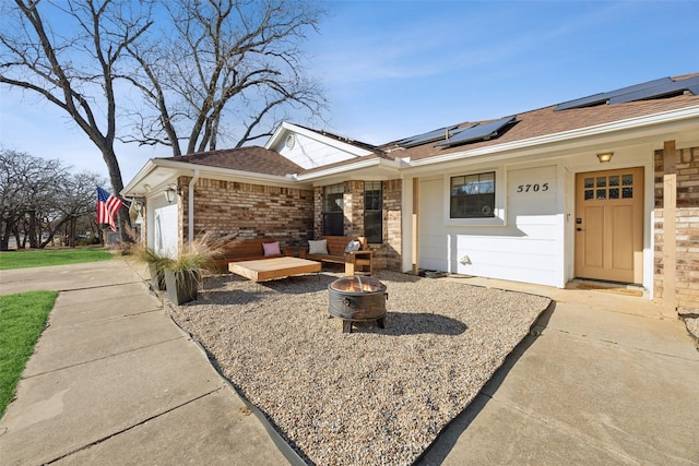 single story home featuring a garage, solar panels, and a fire pit