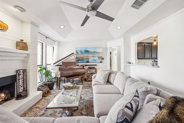 living room with crown molding, a brick fireplace, a raised ceiling, ceiling fan, and light hardwood / wood-style floors