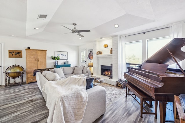 living room featuring ceiling fan, wood-type flooring, a tray ceiling, and a fireplace