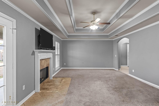 unfurnished living room featuring light tile patterned floors, a premium fireplace, ceiling fan, ornamental molding, and a raised ceiling