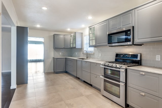 kitchen with crown molding, appliances with stainless steel finishes, sink, gray cabinets, and decorative backsplash