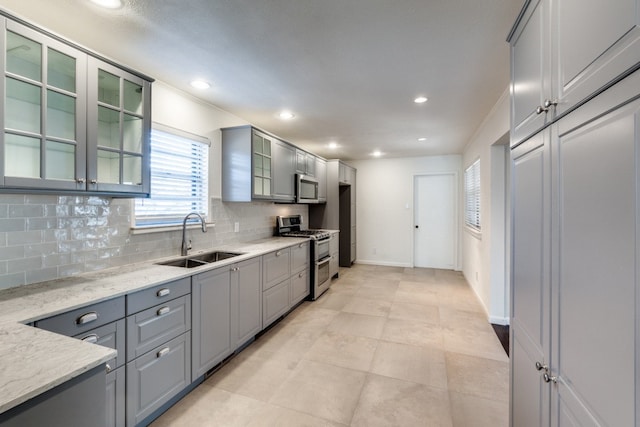 kitchen featuring sink, tasteful backsplash, gray cabinetry, light stone countertops, and stainless steel appliances