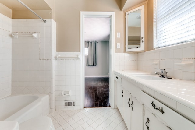 full bathroom with a healthy amount of sunlight, tile patterned flooring, vanity, and tile walls