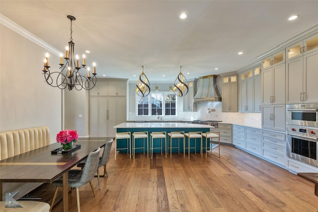 kitchen with pendant lighting, premium range hood, ornamental molding, light hardwood / wood-style floors, and decorative backsplash