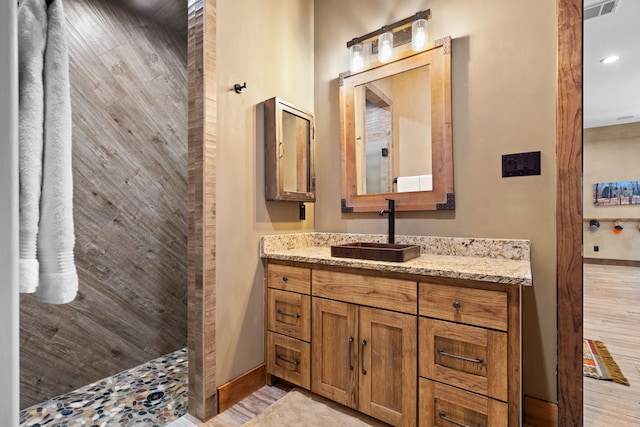 bathroom featuring a walk in shower, baseboards, vanity, and wood finished floors