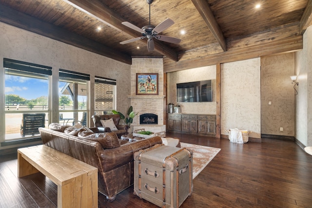 living area with dark wood-style flooring, beamed ceiling, wood ceiling, a large fireplace, and a ceiling fan