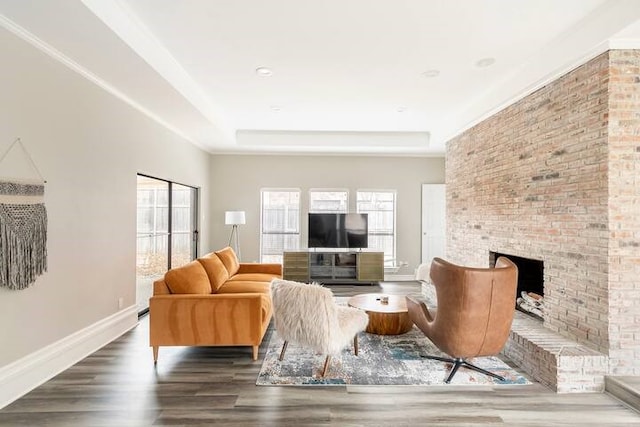 living room featuring dark hardwood / wood-style floors, a tray ceiling, and a brick fireplace