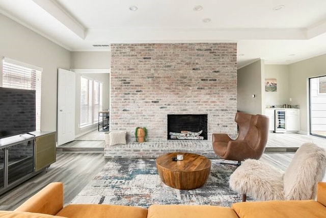 living room with hardwood / wood-style floors, a tray ceiling, ornamental molding, and a brick fireplace