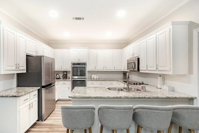 kitchen with appliances with stainless steel finishes, white cabinets, light stone counters, and light hardwood / wood-style flooring