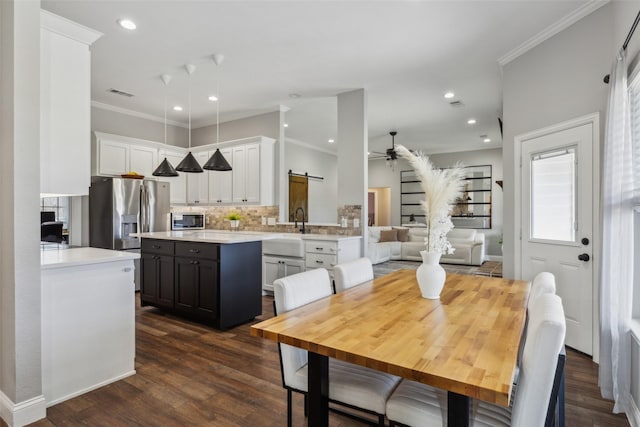 dining space featuring sink, crown molding, dark hardwood / wood-style flooring, ceiling fan, and a barn door