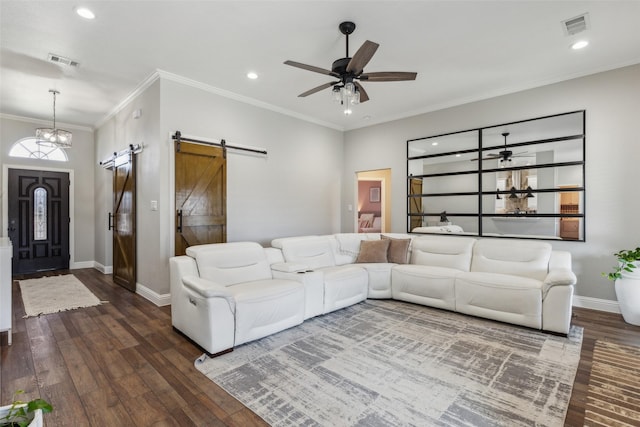 living room featuring dark hardwood / wood-style floors, ceiling fan with notable chandelier, ornamental molding, and a barn door