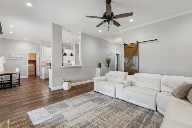 living room featuring dark wood-type flooring, washer / dryer, crown molding, ceiling fan, and a barn door