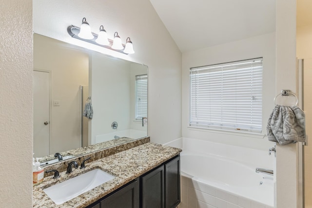 bathroom with vanity, vaulted ceiling, and a relaxing tiled tub