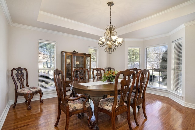 dining area featuring an inviting chandelier, wood-type flooring, and a raised ceiling