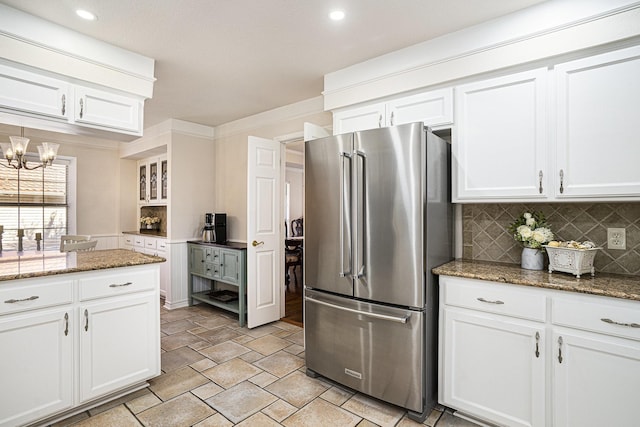 kitchen with stainless steel refrigerator, an inviting chandelier, tasteful backsplash, white cabinets, and dark stone counters