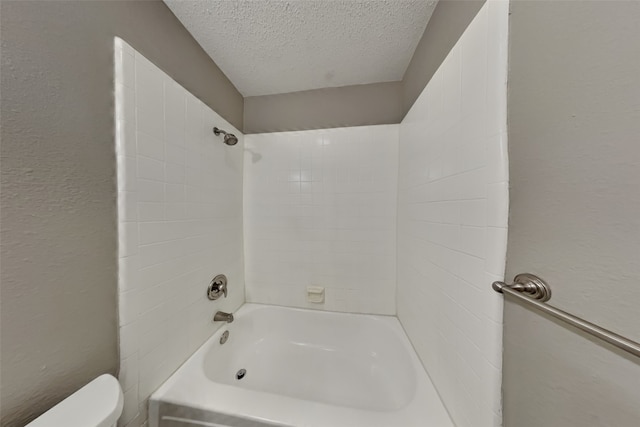 bathroom with toilet, a textured ceiling, and tiled shower / bath