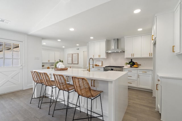 kitchen featuring sink, white cabinets, range, wall chimney range hood, and an island with sink