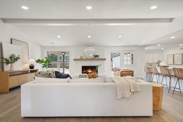 living room with light hardwood / wood-style floors, lofted ceiling with beams, and a brick fireplace