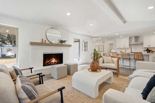 living room with a brick fireplace, sink, lofted ceiling with beams, and light wood-type flooring