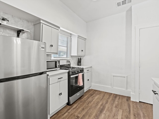 kitchen with white cabinets, light wood-type flooring, appliances with stainless steel finishes, and backsplash