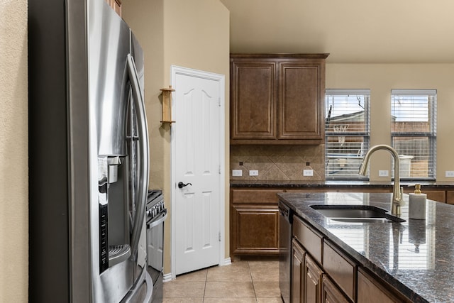 kitchen with stainless steel refrigerator with ice dispenser, dishwasher, sink, light tile patterned floors, and dark stone countertops