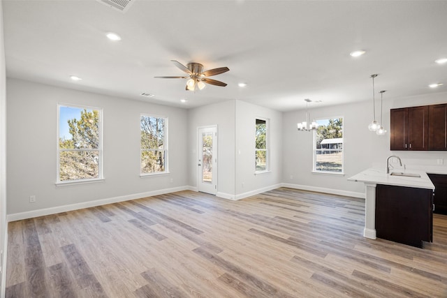 kitchen with a wealth of natural light, sink, light wood-type flooring, kitchen peninsula, and pendant lighting