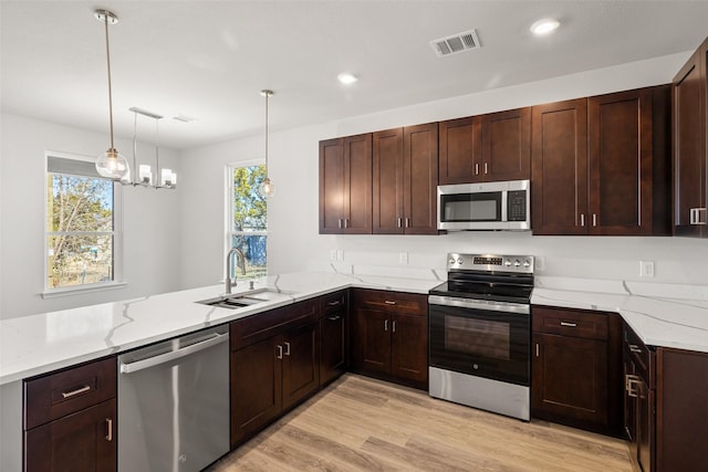 kitchen featuring light hardwood / wood-style floors, sink, kitchen peninsula, pendant lighting, and stainless steel appliances