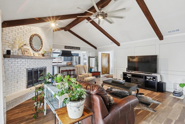 living room with wood-type flooring, ceiling fan, vaulted ceiling with beams, and a brick fireplace