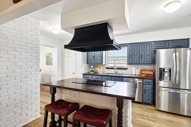 kitchen with sink, blue cabinetry, ventilation hood, wood counters, and stainless steel appliances