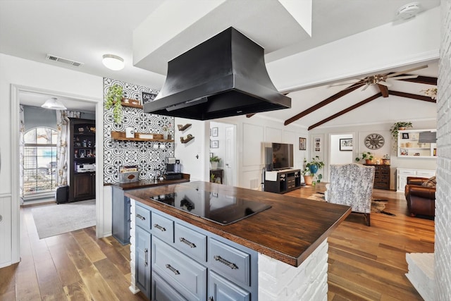 kitchen with hardwood / wood-style floors, butcher block counters, island exhaust hood, lofted ceiling with beams, and black electric cooktop