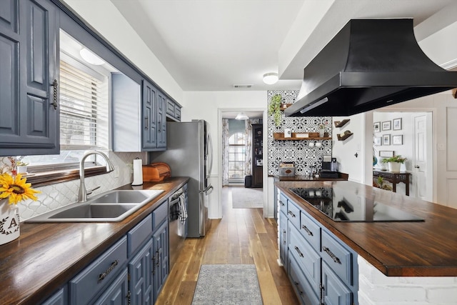 kitchen featuring backsplash, island exhaust hood, blue cabinets, black electric cooktop, and wood counters