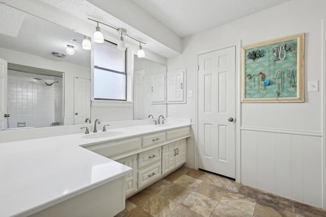 bathroom featuring a textured ceiling, vanity, and a tile shower