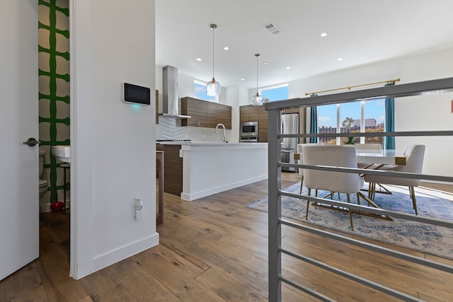 kitchen with pendant lighting, wall chimney range hood, sink, stainless steel appliances, and dark hardwood / wood-style floors