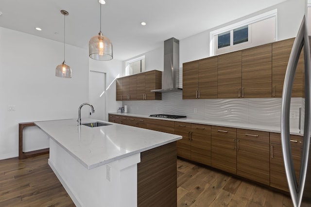 kitchen featuring sink, appliances with stainless steel finishes, a kitchen island with sink, decorative backsplash, and wall chimney range hood