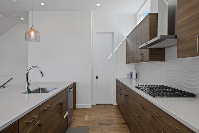 kitchen with pendant lighting, wall chimney range hood, sink, appliances with stainless steel finishes, and light stone countertops