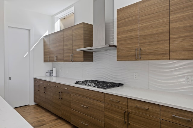 kitchen with tasteful backsplash, wall chimney exhaust hood, stainless steel gas cooktop, and light hardwood / wood-style flooring