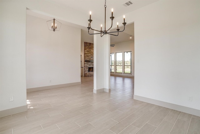 spare room featuring a brick fireplace and a notable chandelier