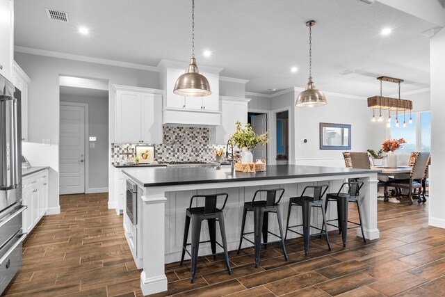 kitchen featuring white cabinets, an island with sink, hanging light fixtures, and a kitchen bar