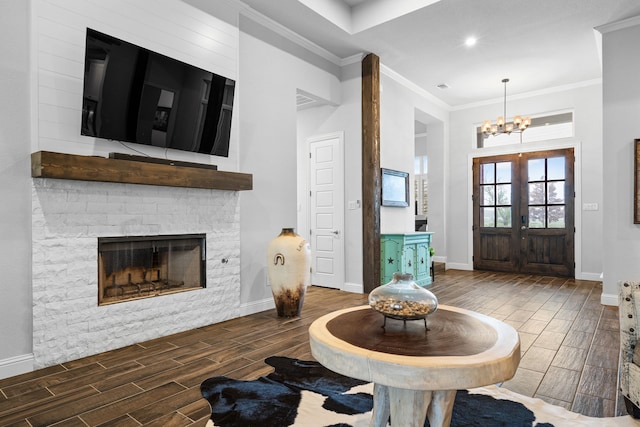 living room with a chandelier, french doors, a stone fireplace, and ornamental molding